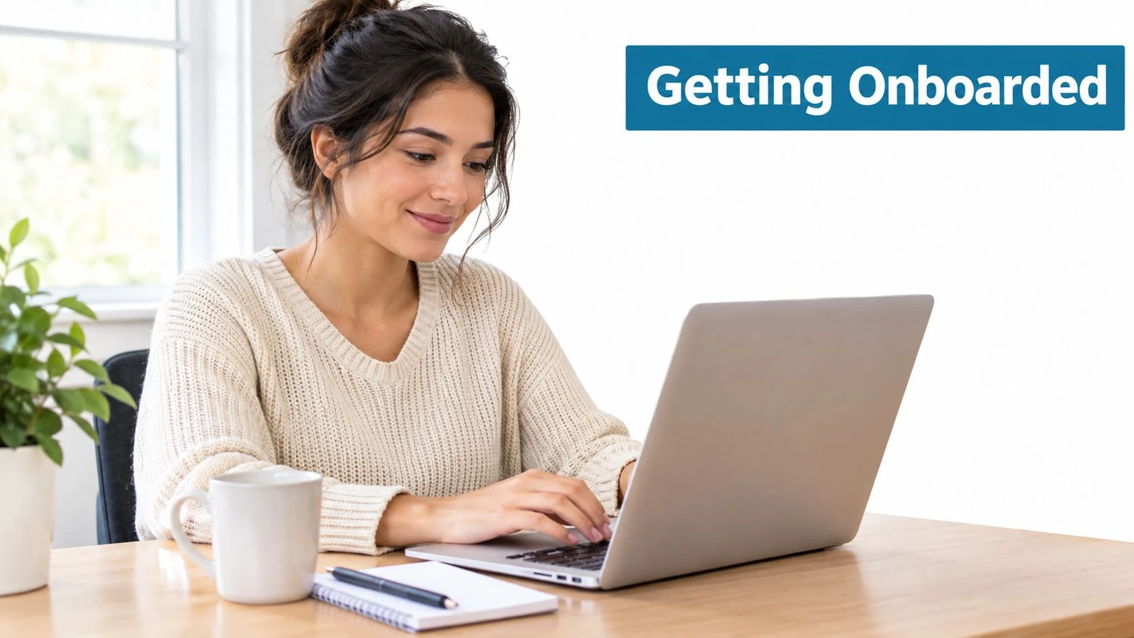 A young woman smiling while working on her laptop at a desk with a coffee mug.