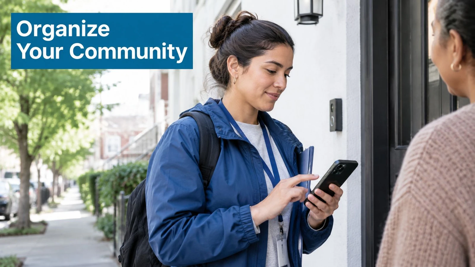 A volunteer with a backpack and a lanyard shows a smartphone screen to a resident at a doorway.